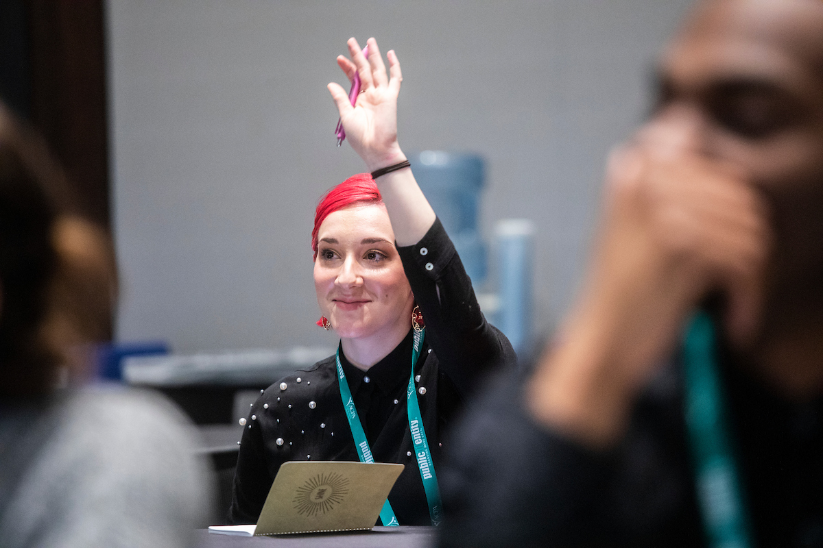 NextGen student raising their hand while sitting down and smiling