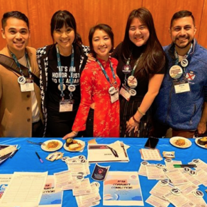 5 APAN leaders standing at a table during ACPA20 handing out buttons and flyers