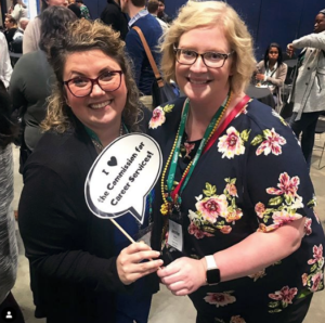two members hold a sign and smile