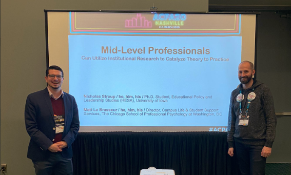 Two mid-level professionals standing in front of a projector screen smiling before a presentation