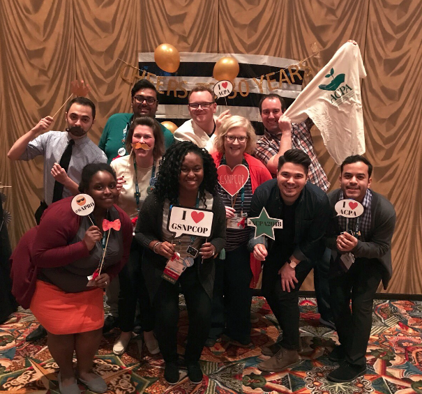 a large group of Graduate Student and New Professional Community of Practice members holding photobooth signs and smiling for a group photo