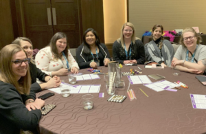 group of women sitting around a round table with papers and pens