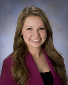 A headshot of Crystal Cyr. A smiling White woman wearing a pink blazer.