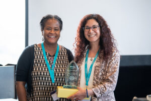 two recipients holding their award and smiling at the camera